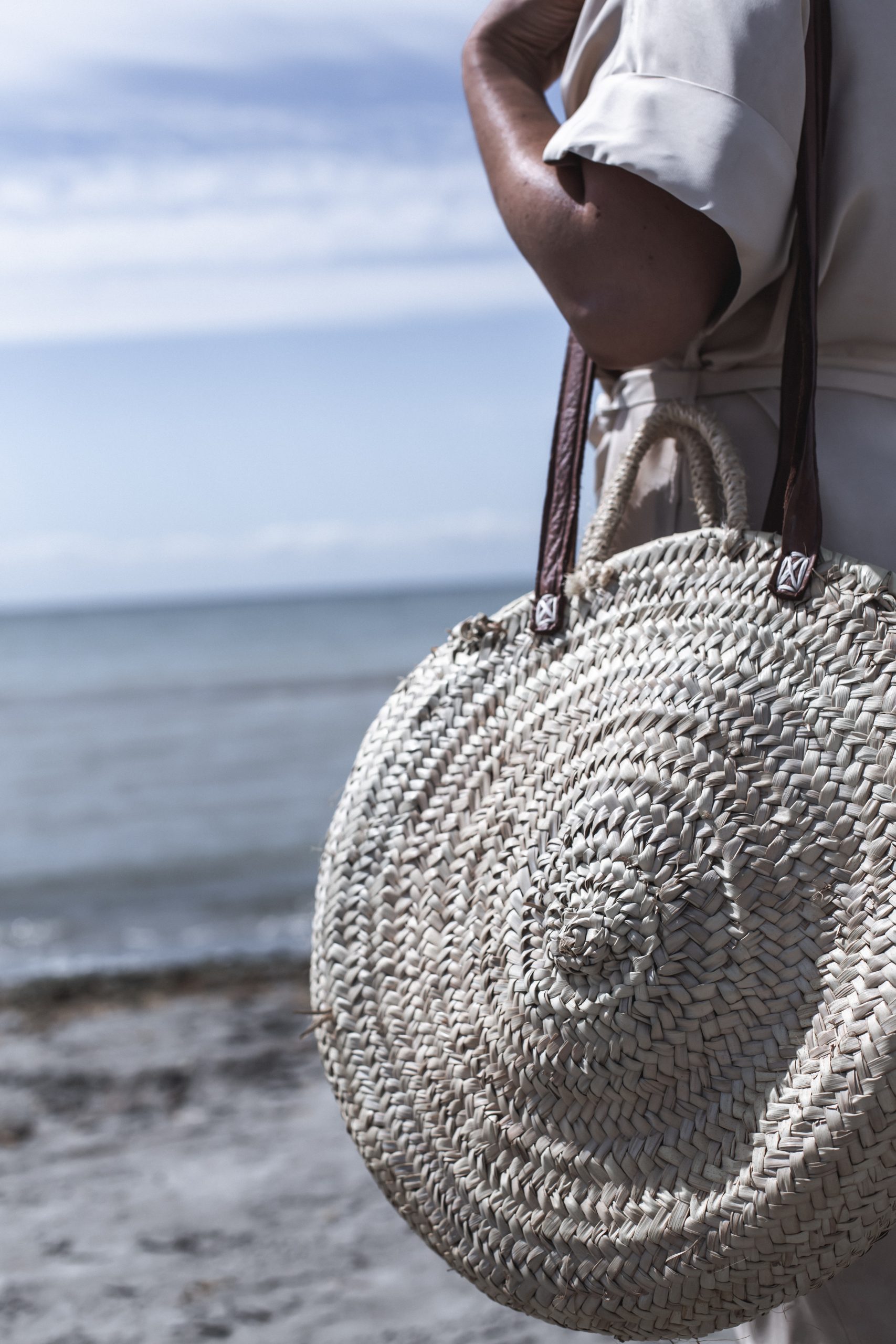 Eva Cruz en la playa vestida con un vestido camisero color nude y un bolso cesta de la firma Wae